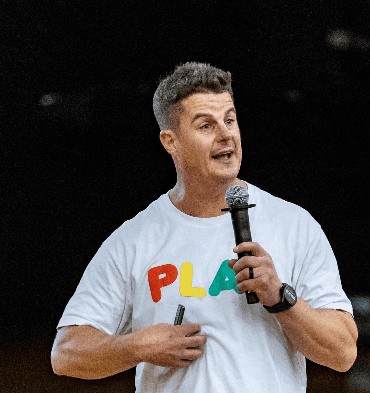 Dale Sidebottom speaking with a microphone in a school hall, wearing a white PLAY t-shirt