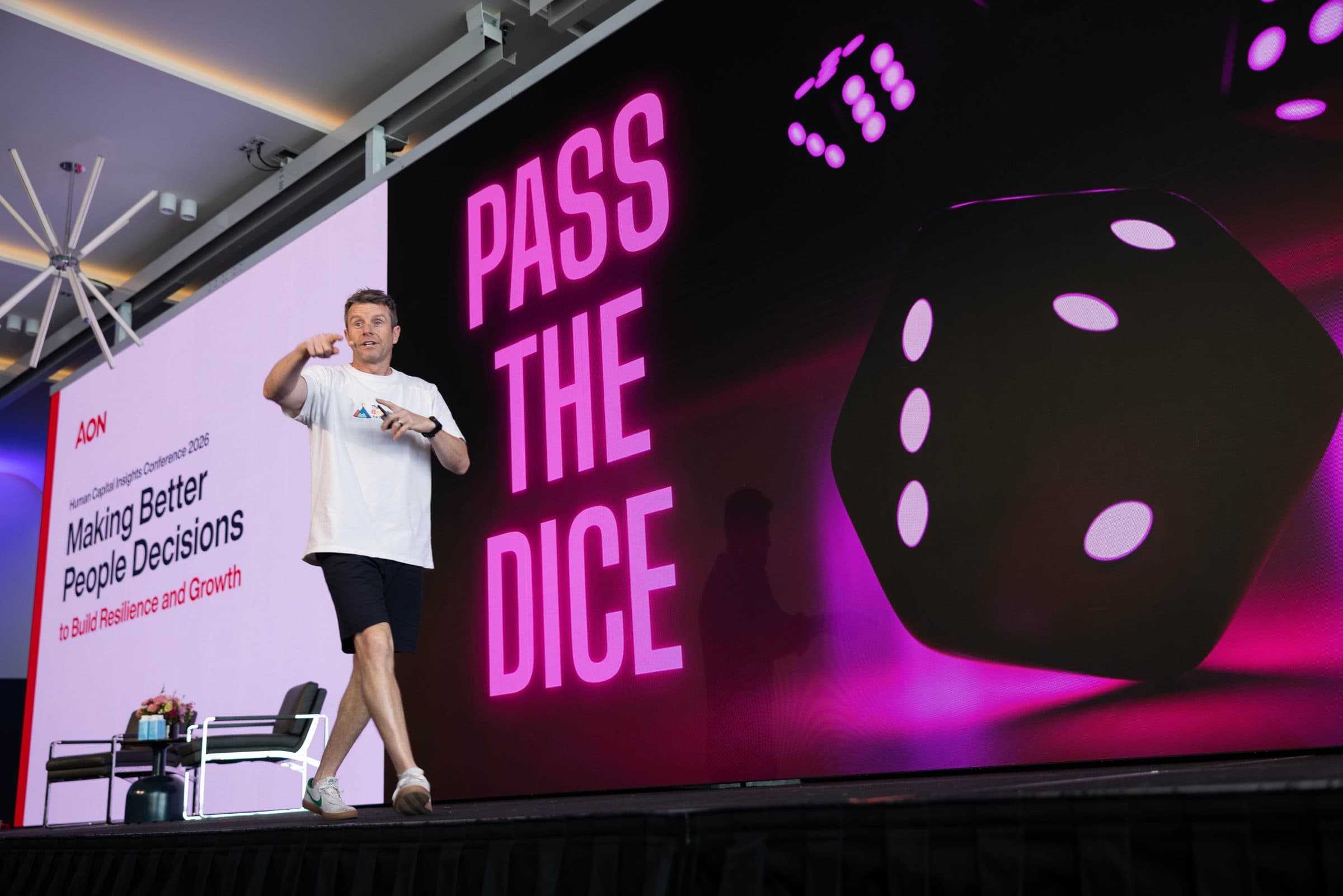 Dale on stage pointing to the audience in front of a giant screen reading Pass the Dice