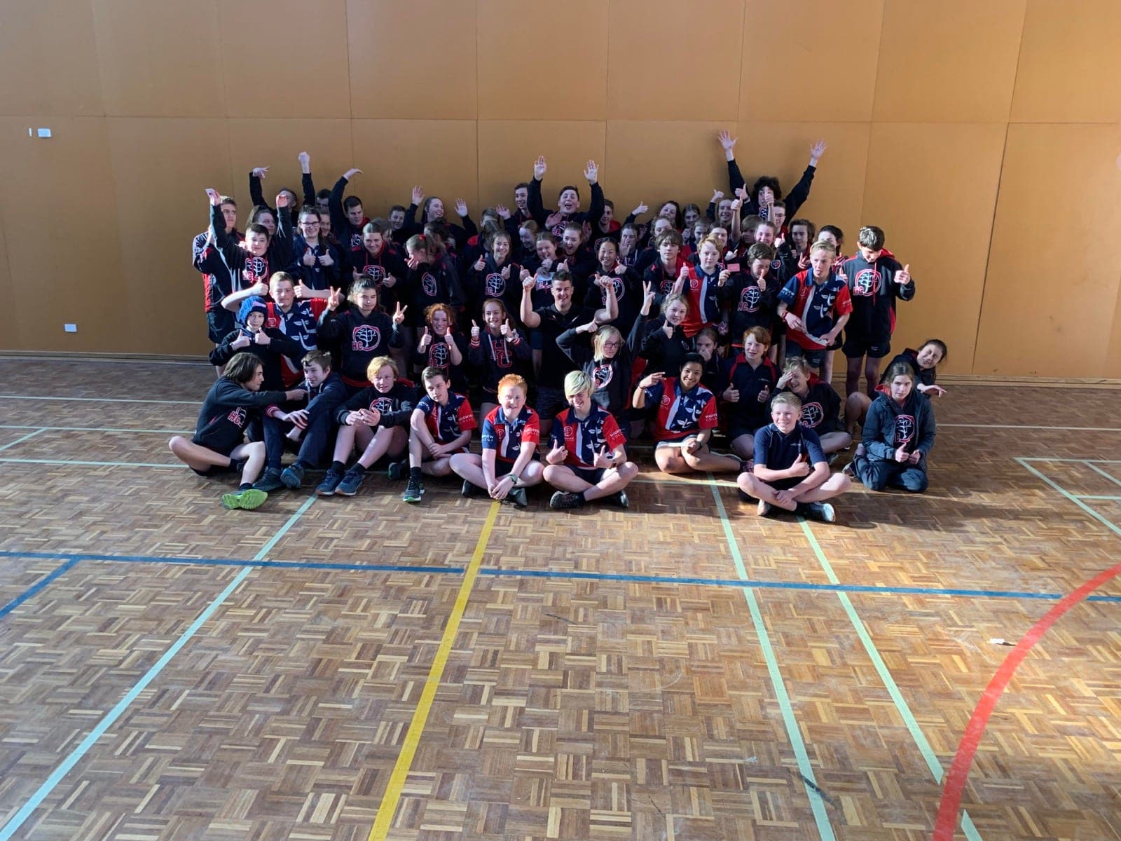 A large group of primary students in uniform cheering together on a gym floor
